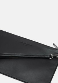 Clutch de cuero negro con superficie texturizada, que cuenta con un cierre de cremallera y una correa de muñeca desmontable. Detalle del logo grabado presente.