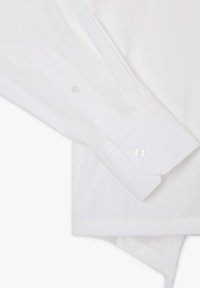 Camicia bianca a maniche lunghe con colletto a punte, caratterizzata da una trama liscia, polsini con bottoni e dettagli di cucitura discreti.