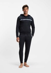 Svart zip-up hoodie med en blå accentrand, matchad med tillhörande avsmalnande mjukisbyxor. Mjukt tyg, ribbade muddar och midjeband.