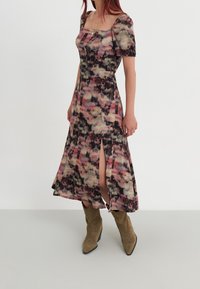 Monivärinen mekko, jossa on neliönmuotoinen pääntie ja lyhyet puffihihat, joissa on virtaava siluetti ja sivurei'itykset, yhdistettynä vaaleanruskeisiin nilkkasääriin.