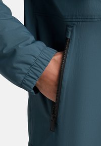 Giacca resistente all'acqua in verde scuro, dotata di una tasca con zip, polsini elastici e una consistenza liscia e leggera.