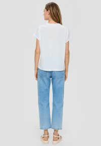 Witte T-shirt met korte mouwen en een relaxed fit, gecombineerd met lichtblauwe rechte jeans en beige sandalen, gezien vanuit de achterkant.