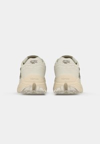 Light-colored synthetic athletic shoes with textured fabric upper, rubber sole featuring a distinct tread pattern, and logo on the heel.