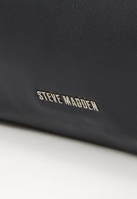 Sac en cuir noir texturé avec un logo argenté "STEVE MADDEN", mettant en avant des surfaces lisses et une forme rectangulaire élancée.