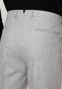 Grijze gestructureerde broek heeft een aansluitende taille, twee achterzakken en een strakke, op maat gemaakte stijl met subtiele stikseldetails.