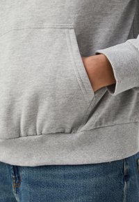 Gray sweatshirt featuring a front pocket, ribbed cuffs, and hem. Fabric texture is soft and slightly brushed, paired with blue jeans.