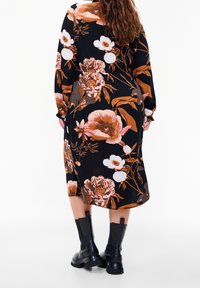Abito floreale con sfondo nero e grandi fiori arancioni e rosa. Maniche lunghe e design di lunghezza media. Stivali neri chunky.