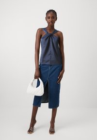 Marineblå satengsinglet uten ermer med vridd frontdetalj, kombinert med en denim midiskjørt med frontslitt og en hvit quilted veske.