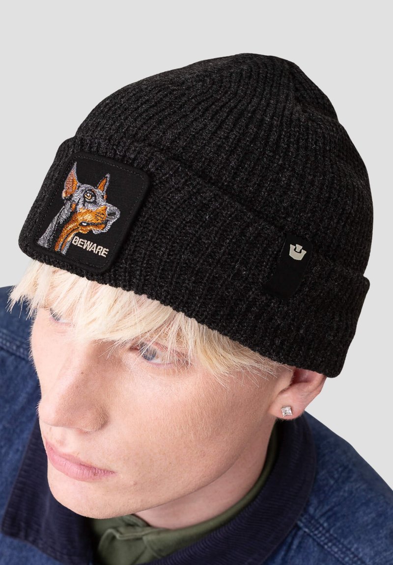 Black knitted beanie with a tight ribbed texture, featuring an embroidered dog graphic and "BEWARE" on a rectangular patch.