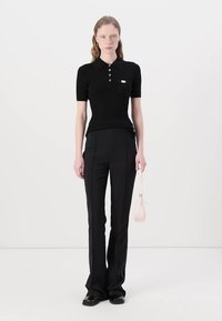 Polo-shirt noir à côtes avec des manches courtes et trois boutons dorés. Assorti à un pantalon noir évasé et un petit sac à main rose.