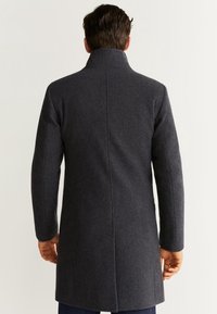 Abrigo de lana gris oscuro con un alto cuello y un corte ajustado, que presenta una costura trasera recta y mangas largas.
