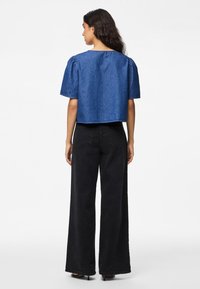 Τζιν κοντό τοπ σε μεσαίο μπλε με φουσκωτά μανίκια, συνδυασμένο με μαύρα παντελόνια σε φαρδιά γραμμή. Απλός σχεδιασμός με ακατέργαστο τελείωμα και μινιμαλιστικές λεπτομέρειες.