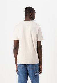 T-shirt en coton beige clair à coupe régulière, manches courtes et design de yoke au dos, associé à un pantalon cargo en denim bleu.
