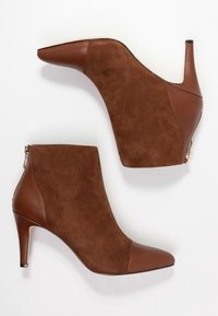 Botas tobilleras marrones que combinan cuero liso y ante, con punta afilada, tacón alto y detalle de cremallera lateral.