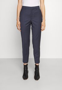 Pantalon tailleur marine à coupe slim, avec plis avant et longueur mi-mollet. Confectionné dans un tissu lisse, associé à des bottines noires.