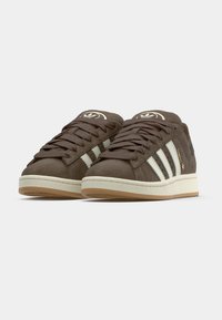 Baskets en daim marron avec des rayures blanches, bout arrondi, semelle plate en gomme et lacets texturés. Présentent un logo sur la languette et le panneau latéral.