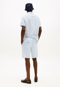 Camicetta azzurra a maniche corte in tessuto testurizzato, abbinata a pantaloni corti azzurri con tasche e un cappello a secchiello blu navy. Scarpe marroni.