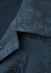 Mörkblått tyg med en subtil blommönster, med en jämn textur och en något upphöjd design. Skräddarsydd krage visas.