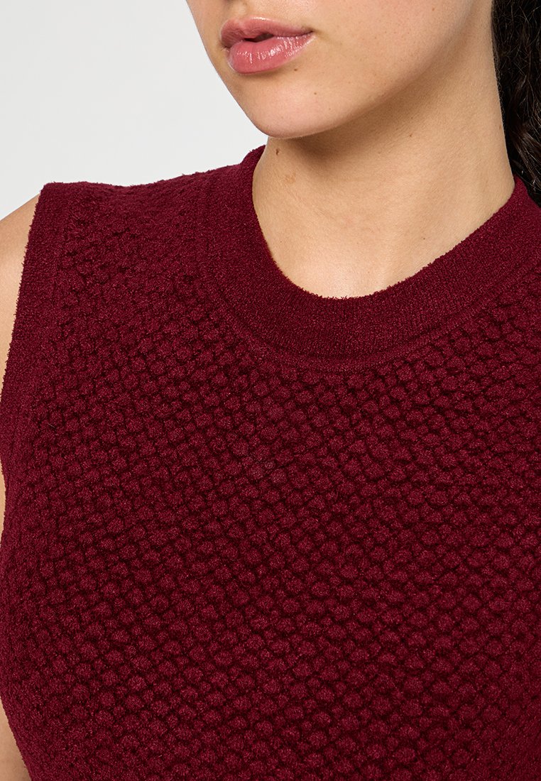 Top sin mangas de color burdeos que presenta un patrón de punto texturizado en forma de burbujas y un cuello acanalado. Tela suave con un aspecto cálido y acogedor.