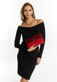 Pochette rossa con dettagli in piume, texture lucida e design piatto. Il modello indossa un vestito nero senza spalline e una collana a catena dorata.