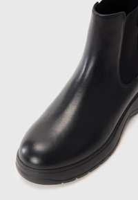 Bottine en cuir noir à bout rond, avec des panneaux élastiques sur les côtés et une semelle en caoutchouc texturée. Finition lisse avec un minimum de couture.