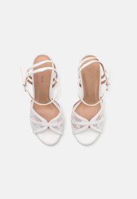 Sandales à talons blancs avec des lanières croisées en dentelle et une finition satinée lisse, dotées d'une sangle �à la cheville et d'une semelle rembourrée.