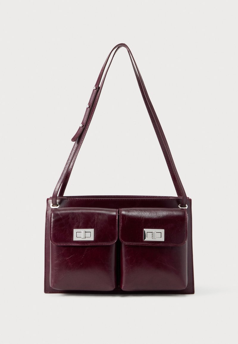 Σκούρα βαθυκόκκινη δερμάτινη τσάντα ώμου με δύο εμπρόσθιες τσέπες με καπάκι και ασημί ορθογώνια κλειδώματα περιστροφής. Ρυθμιζόμενο λουρί με ασημί κουμπιά.