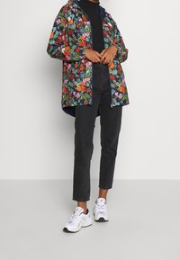 Kolorowa, wodoodporna kurtka w kwiatowy wzór z kapturem, zestawiona z czarnymi spodniami i białymi trampkami. Posiada zamek błyskawiczny z przodu oraz kieszenie.