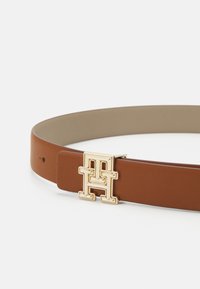 Cintura in pelle marrone con fibbia rettangolare dorata con logo 'H'. Texture liscia senza motivi o decorazioni visibili.