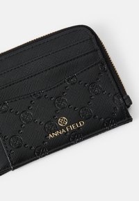 Black wallet with textured fabric, embossed floral pattern, gold logo, and multiple card slots. Zipper closure along the top edge.