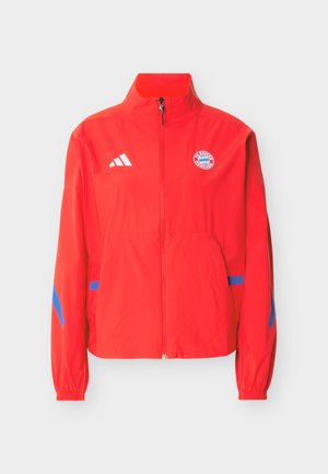 Κόκκινο μπουφάν με πλήρες φερμουάρ, με το λογότυπο της FC Bayern Munich στο στήθος, το λογότυπο της Adidas στο αντίθετο μέρος και μπλε λεπτομέρειες στα μανίκια και τις τσέπες.