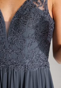 Graues Kleid mit aufwendiger floraler Stickerei und Perlenverzierung. Der Oberteil hat einen tiefen V-Ausschnitt und eine durchsichtige Überlage mit einem fließenden, plissierten Rock.