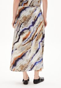Lange rok met een vloeiende ontwerp in beige, crème en blauwe marmerpatronen. Gemaakt van gladde stof, heeft een tailleband en zwarte schoenen.