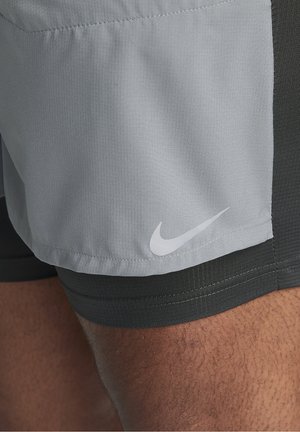 Nahaufnahme von grauen und schwarzen, mehrlagigen Sportshorts mit weißem Nike-Swoosh auf der grauen Außenschicht, getragen am Oberschenkel einer Person.