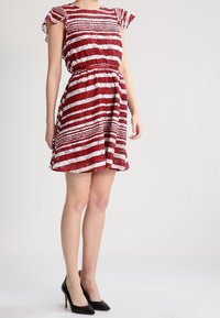 Robe rayée rouge et blanche avec manches courtes à volants, taille cintrée et jupe évasée. Tissu léger et à motifs. Escarpins noirs.