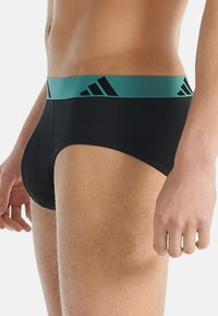 Czarne majtki z turkusowym paskiem w talii, zdobione czarnymi logo Adidas, wykonane z gładkiego, elastycznego materiału zapewniającego komfort i dopasowanie.