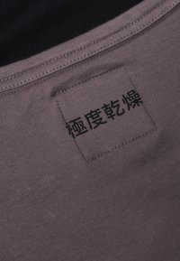 Grått tyg med en slät textur och synlig sömnad, med en fyrkantig etikett med svart text som indikerar tvättråd.