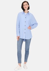 Camicia button-up a righe blu chiaro con maniche lunghe, tasca sul petto, abbinata a jeans slim-fit e sneakers bianche.