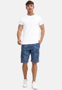 Men's white crew-neck t-shirt paired with blue cargo shorts featuring a floral pattern. Notable details: pockets and textured fabric. White sneakers.