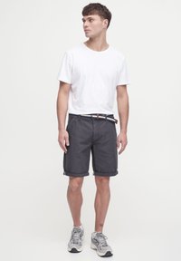 Gray cotton shorts with rolled hem, featuring side pockets and a woven belt. Paired with a simple white t-shirt and light sneakers.