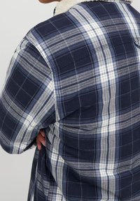 Marinblå och vit rutig skjorta med en mjuk krämfärgad sherpa-krage, med långa ärmar och en avslappnad passform. Texturerad tyg med växelvisa ränder.