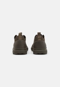 Zapatos verde oliva oscuro con un diseño texturizado, paneles elásticos y lengüetas traseras. Cuentan con una suela de goma gruesa con un patrón de relieve.