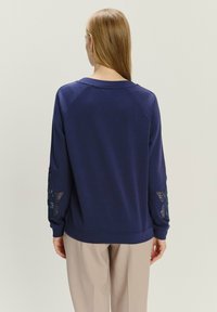 Granatowy sweatshirt z raglanowymi rękawami, ozdobiony floralnym haftem na rękawach oraz okrągłym dekoltem. Wykonany z miękkiego materiału bawełnianego.