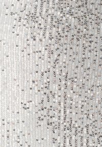 Tessuto in paillettes argento con una superficie testurizzata, caratterizzato da schemi alternati di paillettes circolari in bianco iridescente e tonalità smorzate.