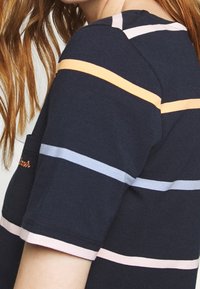 Granatowa bawełniana koszulka z krótkim rękawem, w poziome pasy w jasnoróżowym, pomarańczowym i jasnoniebieskim kolorze. Posiada małą kieszonkę.