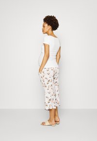 Top justo de mangas curtas em branco combinado com calças cropped de estampado floral em tons pastéis; tecido texturizado visível, com bolsos laterais e sandálias de salto aberto.