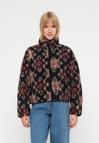 Chlupatá zipová bunda s černým, růžov�ým a bordó květinovým vzorem, vysokým límcem a volným střihem. Kombinována s světle modrými džíny.