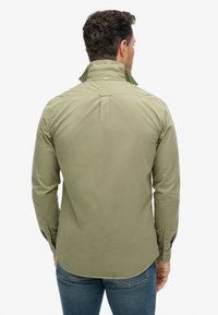 Camisa de manga larga en verde oliva, con un cuello alto, puños abotonados y corte recto, fabricada en una tela suave y ligera.