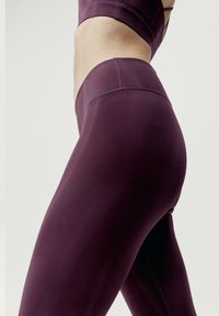 Vysoké fialové sportovní legíny z hladkého, elastického materiálu s tonálním šitím a konturovým střihem.