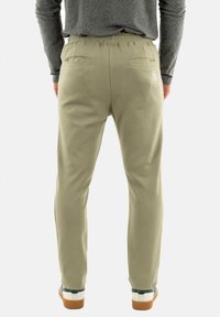 Lys khaki joggers med elastisk talje, to baglommer og struktureret stof, parret med hvide og grønne sneakers.